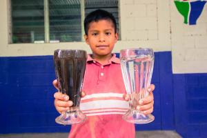 A local boy holds two glasses of water, demonstrating the difference between locally sourced water and a glass of water passed through the purifying filter brought to his community by The WaterVan project.